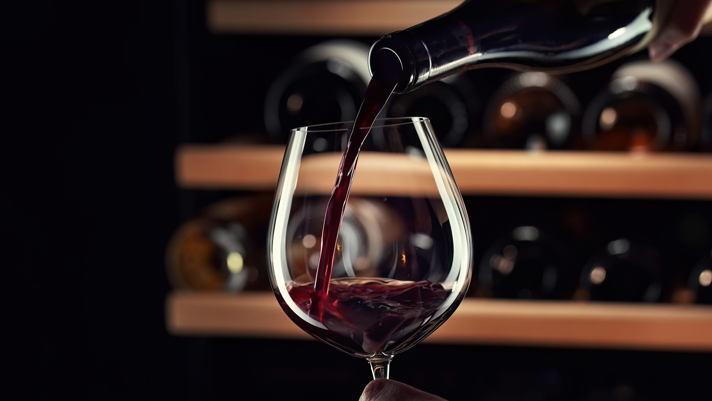 Red wine being poured into a glass in a wine cellar